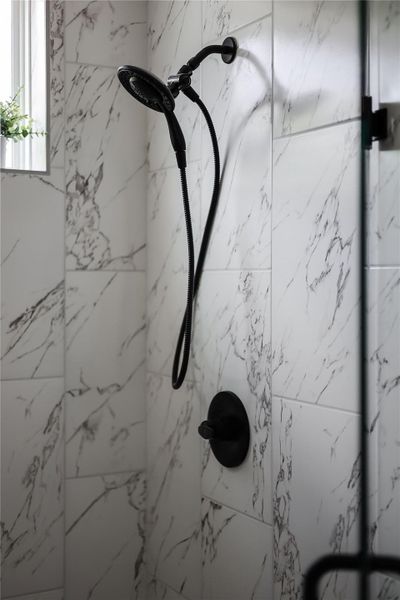 Marble-look tile walls with contrasting matte black shower fixtures create a striking modern aesthetic.