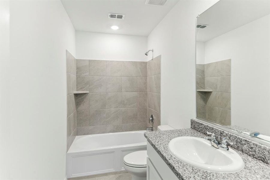 Full bathroom featuring vanity, tiled shower / bath combo, and toilet