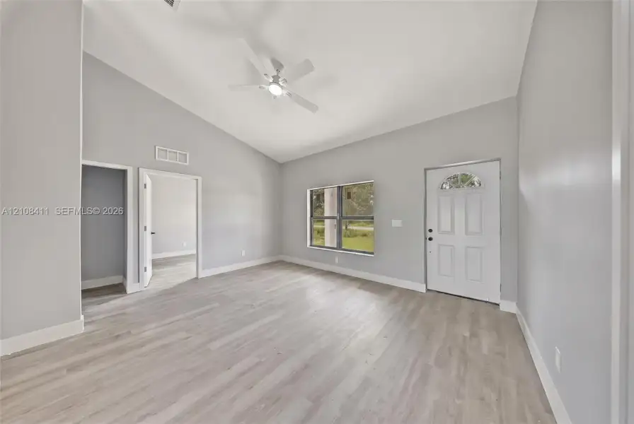 Interior space featuring vaulted ceilings, wood-finish flooring, a ceiling fan, and a six-panel exterior door with an arched glass insert