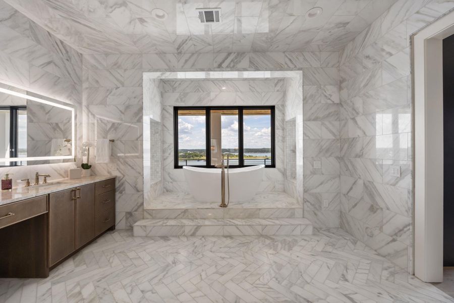 A lavish bath features a soaking tub and a vanity with an illuminated mirror, all surrounded by luxurious marble. A lavish bath features a soaking tub and a vanity with an illuminated mirror, all surrounded by luxurious marble.