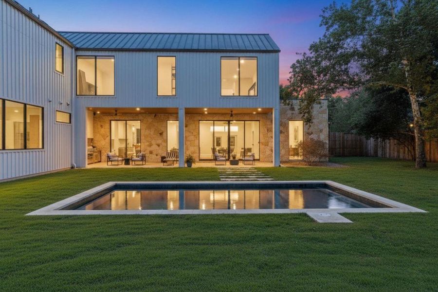 Back of property at dusk with a patio area, stone siding, a yard, and a metal roof Back of property at dusk with a patio area, stone siding, a yard, and a metal roof