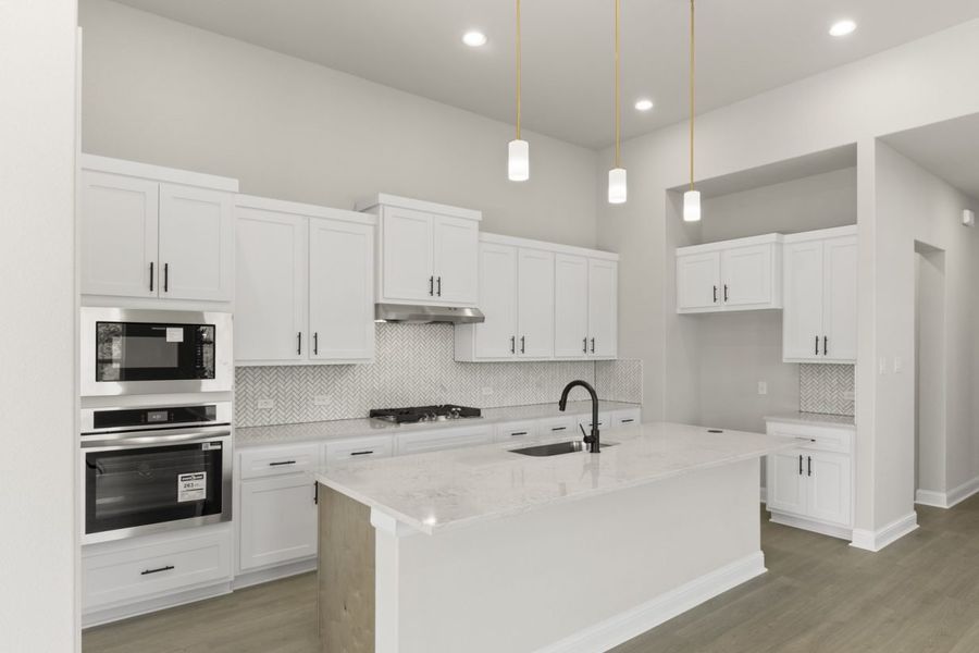 Image of a two story home kitchen with white cabinets, a center island, stainless steel appliances and white backsplash