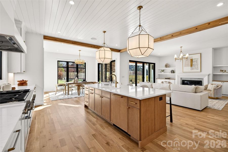 View of the open living space from the Kitchen. Gorgeous lighting. Center Island that can accommodate four bar stools. Gas Thermadore stove on left. Looking toward the FP with mantel and bookcases.