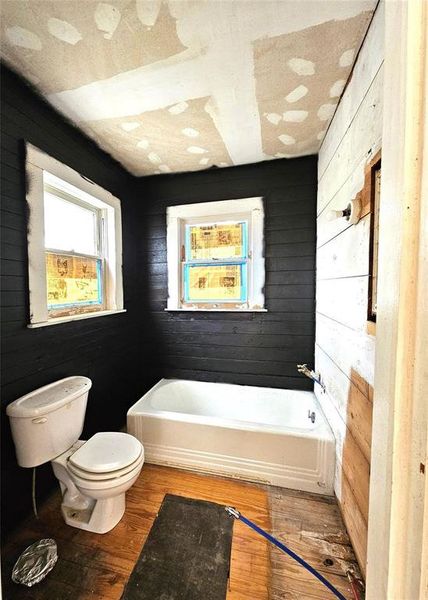 Bathroom with a bathing tub, wood walls, toilet, and hardwood / wood-style flooring Bathroom with a bathing tub, wood walls, toilet, and hardwood / wood-style flooring