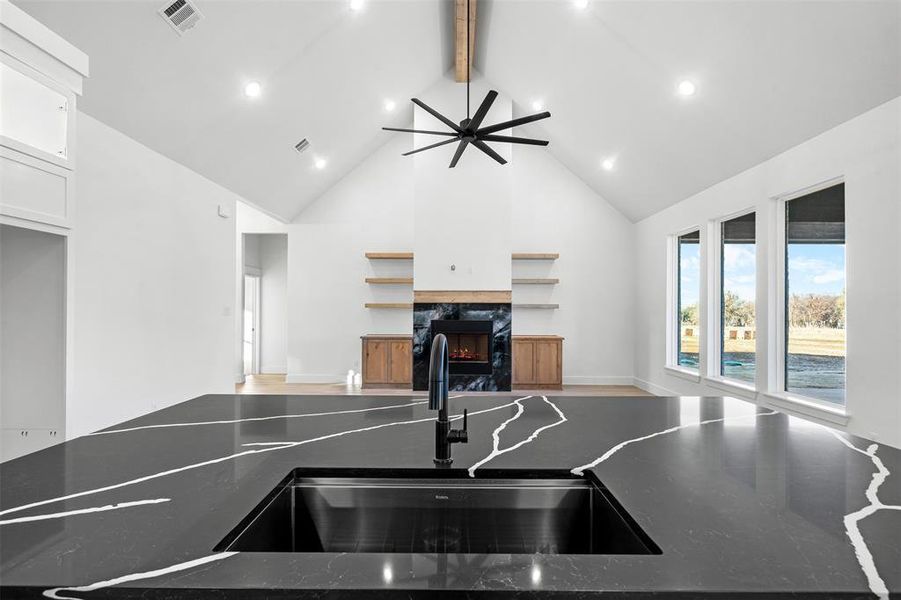 Kitchen featuring white cabinets, a fireplace, dark stone countertops, and beamed ceiling