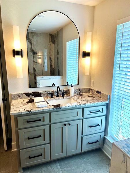 Bathroom featuring vanity, a marble finish shower, and a textured wall Bathroom featuring vanity, a marble finish shower, and a textured wall
