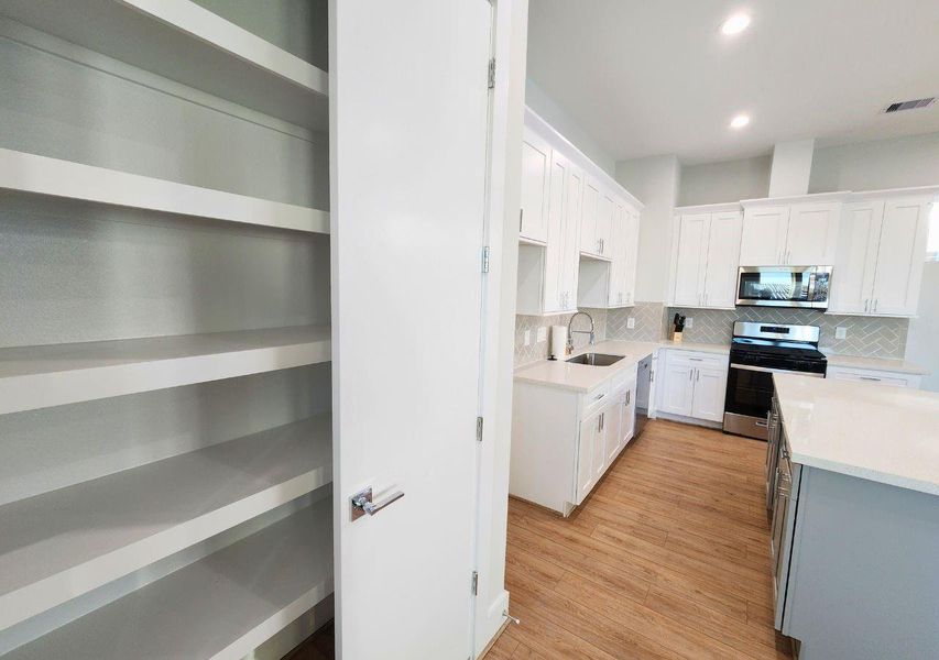 Modern kitchen with white cabinetry, stainless steel appliances, and wood flooring. Features a spacious pantry and ample counter space. Modern kitchen with white cabinetry, stainless steel appliances, and wood flooring. Features a spacious pantry and ample counter space.
