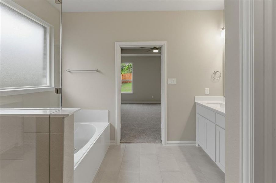 Spacious bathroom featuring light-toned tile flooring, a built-in bathtub, a walk-in shower with frosted window, and a vanity with an undermount sink