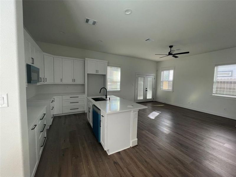 Kitchen with white cabinetry, an island with sink, dark wood-style flooring, open floor plan, and black microwave