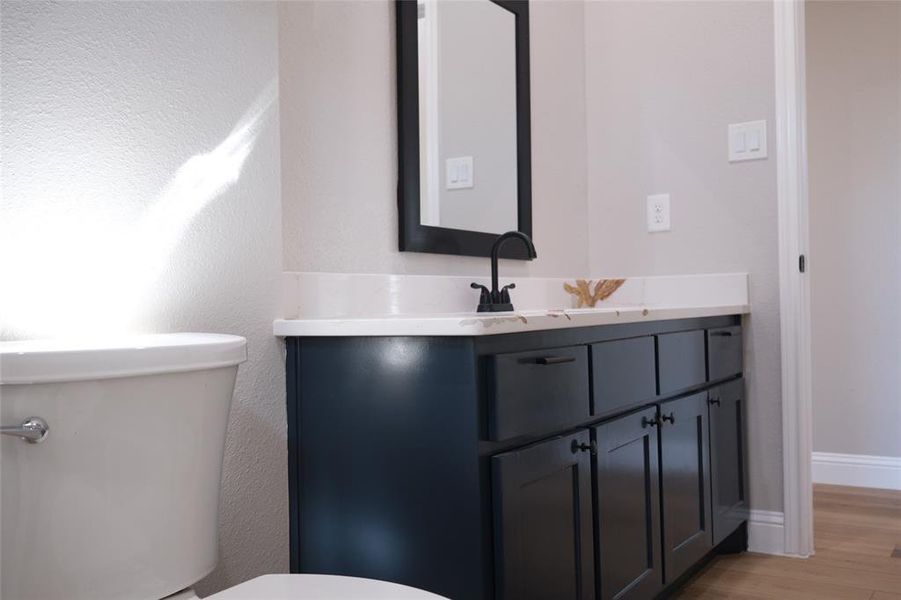 Half bathroom with vanity, light wood-style flooring, and a textured wall Half bathroom with vanity, light wood-style flooring, and a textured wall