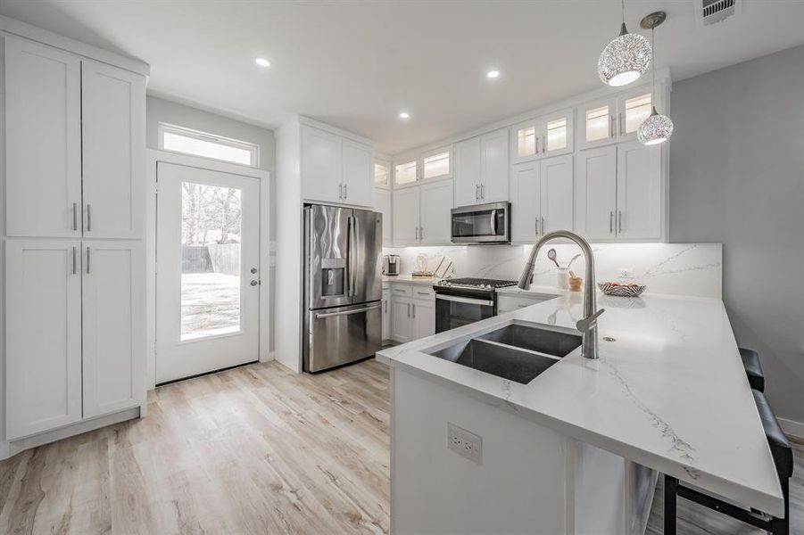 Kitchen featuring pendant lighting, kitchen peninsula, white cabinets, and appliances with stainless steel finishes