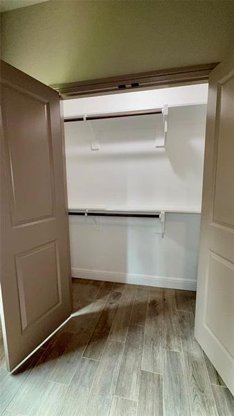 Spacious closet featuring wood-finish flooring, white walls, and built-in shelving with two clothing rods Spacious closet featuring wood-finish flooring, white walls, and built-in shelving with two clothing rods