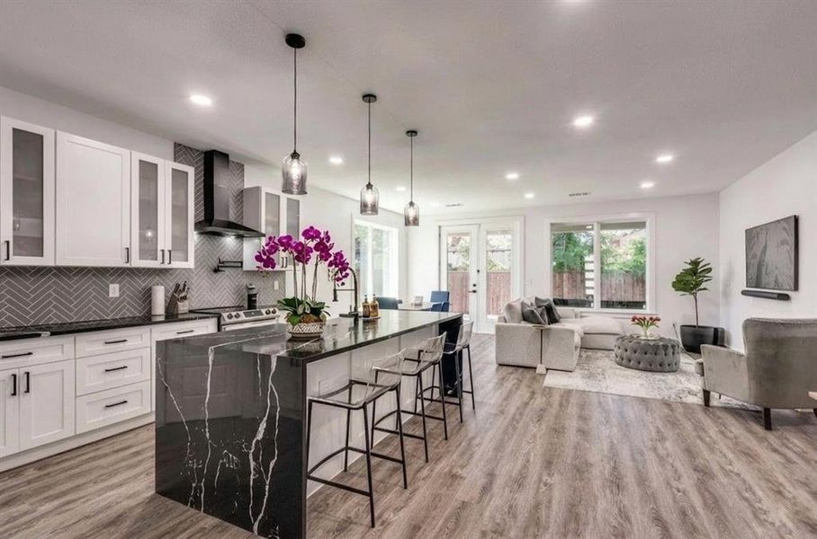 Kitchen with wall chimney exhaust hood, a kitchen bar, open floor plan, backsplash, and light wood finished floors