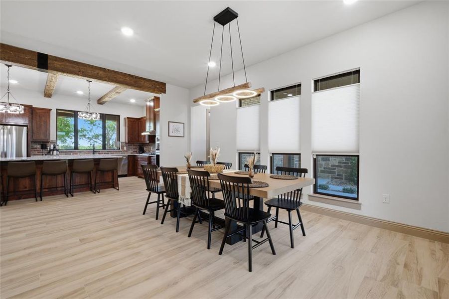 Open-concept living space with light wood-finish flooring, featuring a dining area with a modern linear chandelier