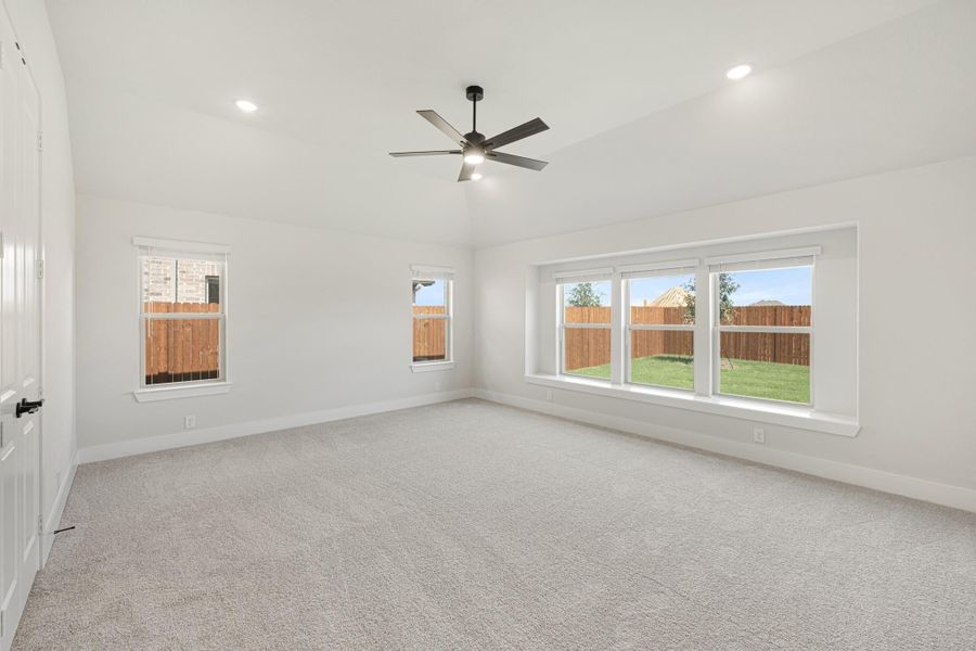 Empty bedroom with carpet, ceiling fan, and multiple windows overlooking a fenced backyard