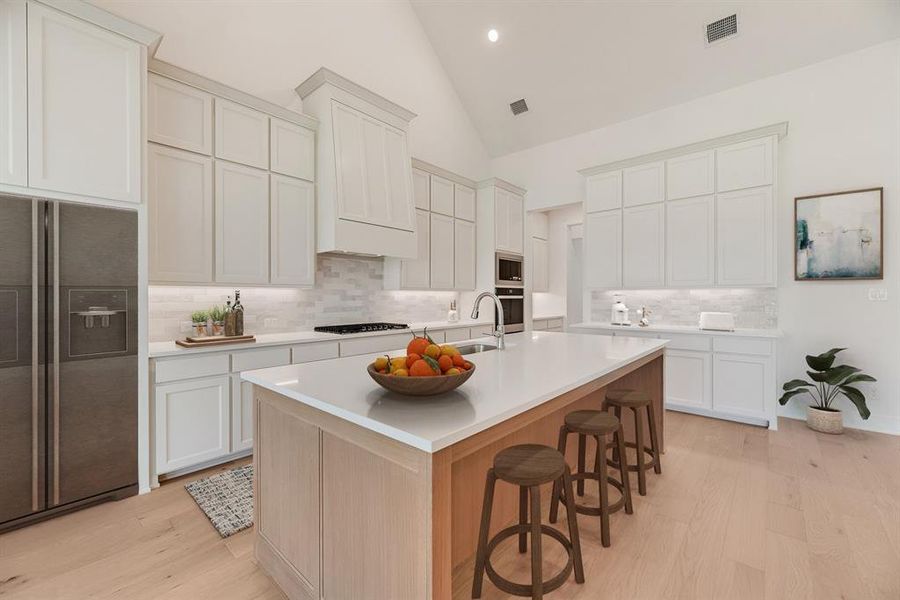 Kitchen with appliances with stainless steel finishes, light wood-type flooring, a kitchen bar, white cabinetry, and high vaulted ceiling