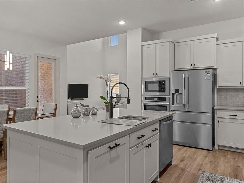 Kitchen featuring stainless steel appliances, sink, white cabinets, an island with sink, and backsplash