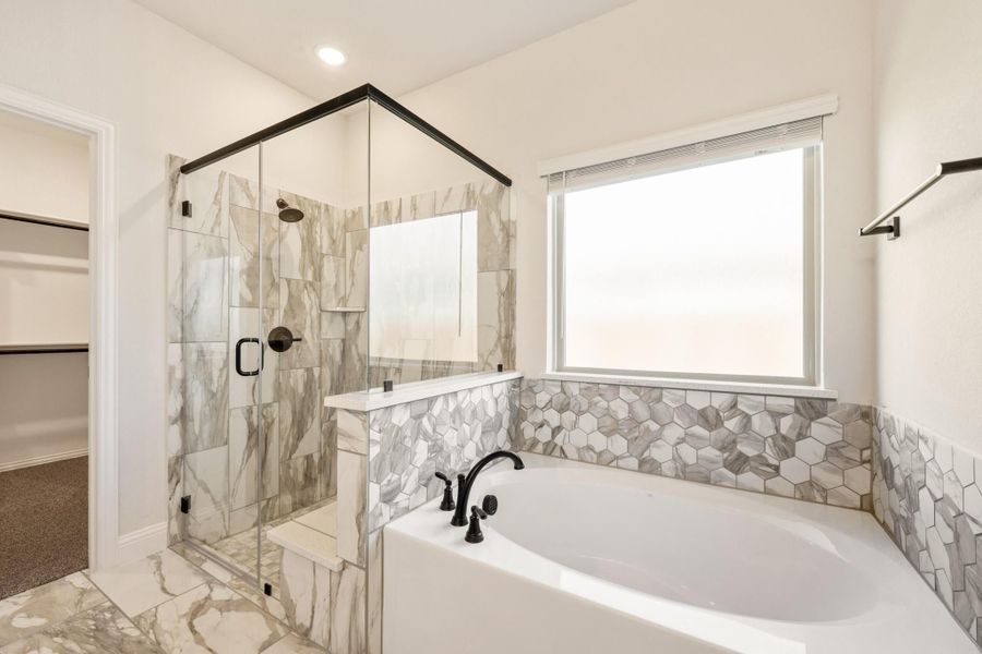 Master bathroom with soaking tub, glass-enclosed shower, marble tile, and walk-in closet entry