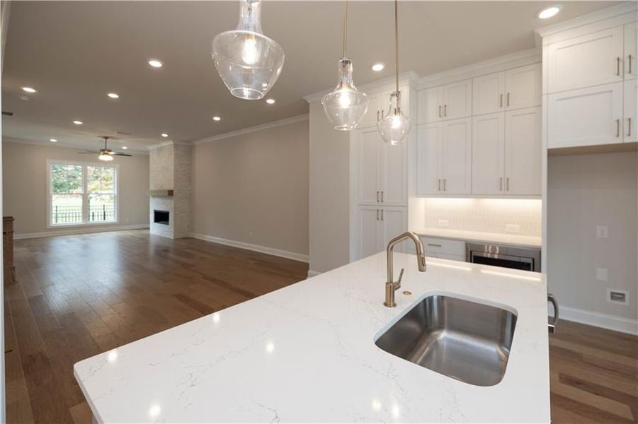 Kitchen featuring sink, white cabinetry, pendant lighting, a fireplace, and light stone countertops