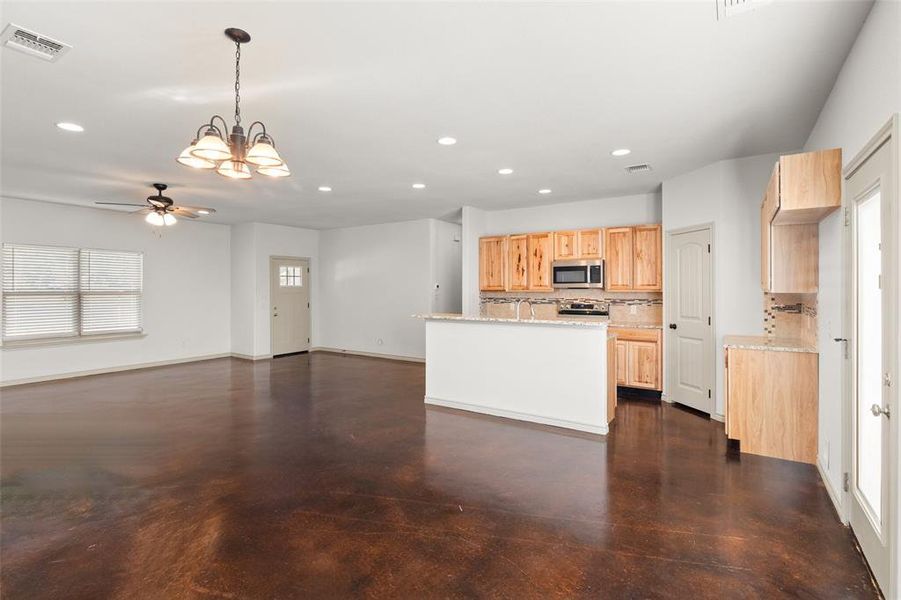 Kitchen with light brown cabinetry, tasteful backsplash, hanging light fixtures, ceiling fan with notable chandelier, and appliances with stainless steel finishes