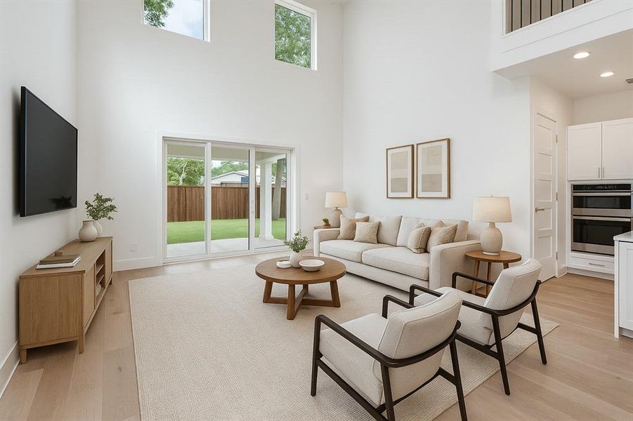 Living area with a high ceiling, plenty of natural light, light wood finished floors, recessed lighting, and baseboards