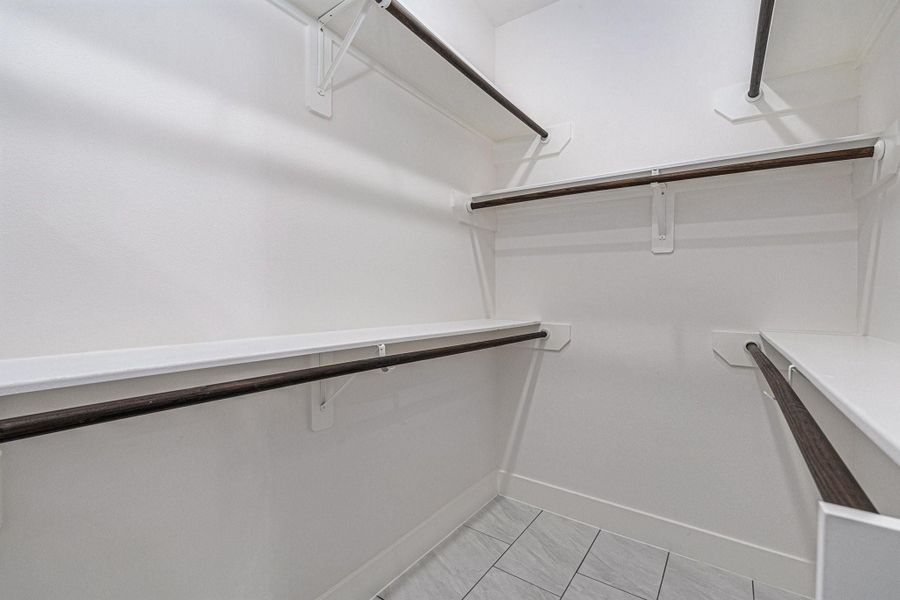 Spacious walk-in closet with multiple shelves and hanging rods, featuring clean white walls and tiled flooring.