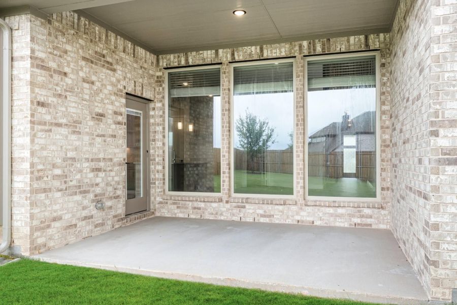 Covered back patio with concrete floor, light brick exterior, large windows, and a glass back door Covered back patio with concrete floor, light brick exterior, large windows, and a glass back door