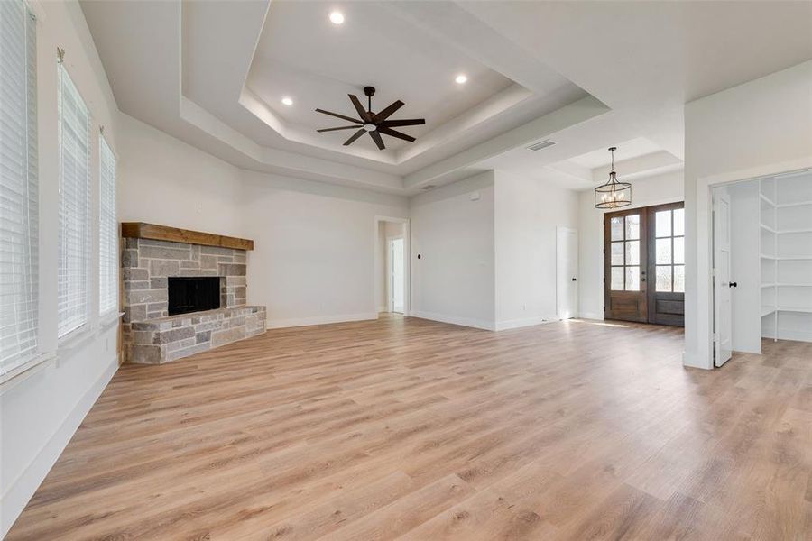 Spacious interior featuring wood-finish flooring, a stone fireplace with a wood mantle, and a tray ceiling with recessed lighting and a ceiling fan