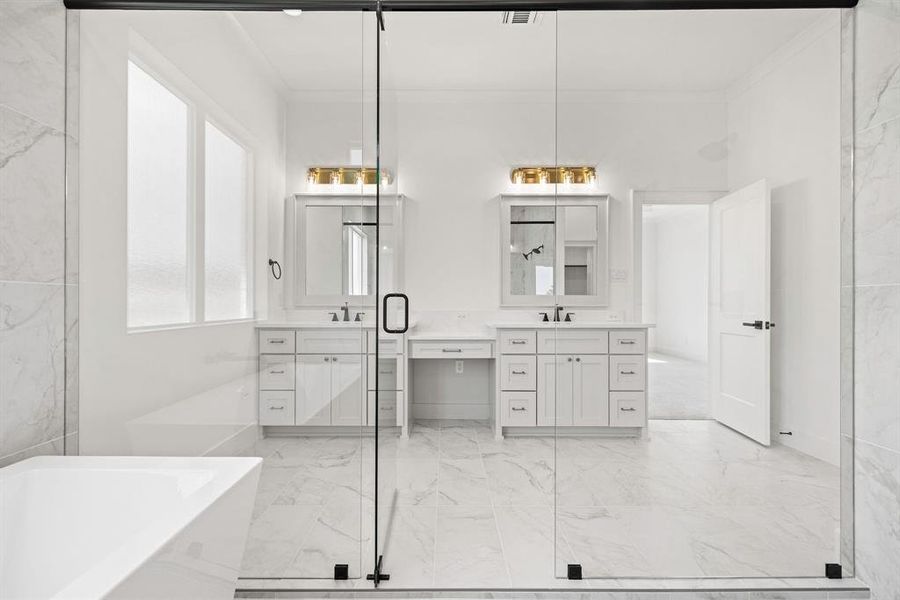Full bathroom featuring marble finish floor, two vanities, a freestanding bath, and a sink