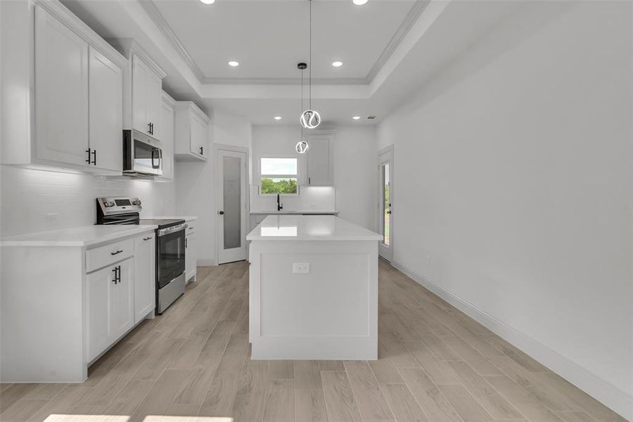 Kitchen featuring stainless steel range with electric stovetop, a raised ceiling, light countertops, a kitchen island, and recessed lighting Kitchen featuring stainless steel range with electric stovetop, a raised ceiling, light countertops, a kitchen island, and recessed lighting