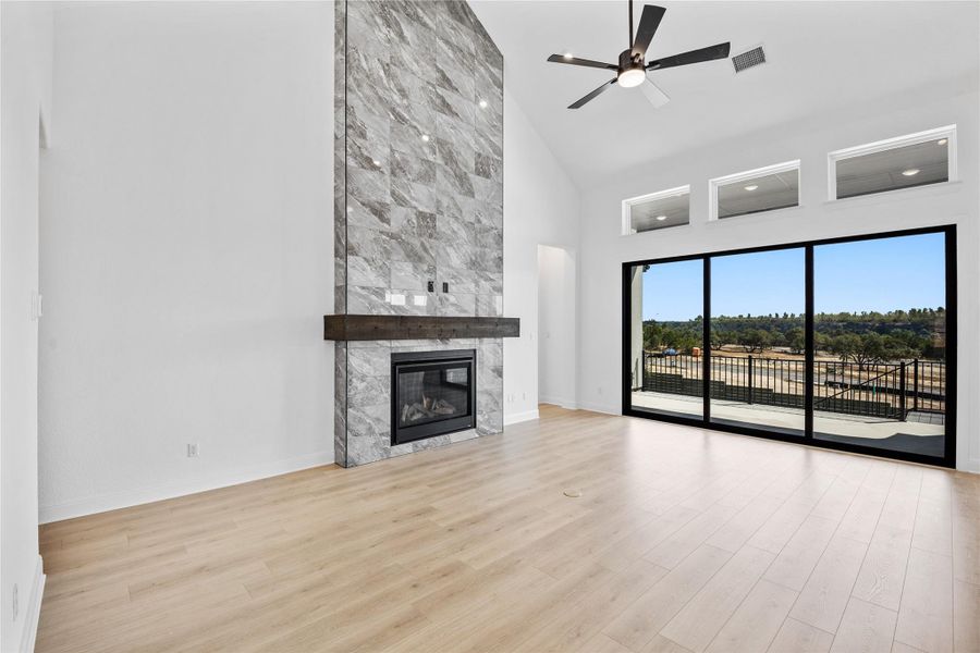 Unfurnished living room featuring light wood-type flooring, ceiling fan, a fireplace, and lofted ceiling