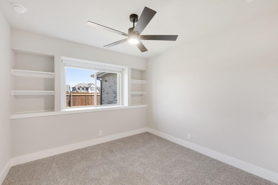 Empty bedroom with built-in wall shelves, ceiling fan, carpet flooring, and a window with neighborhood view