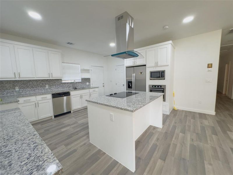 Kitchen with white cabinets, stainless steel appliances, island range hood, light style flooring, and sink