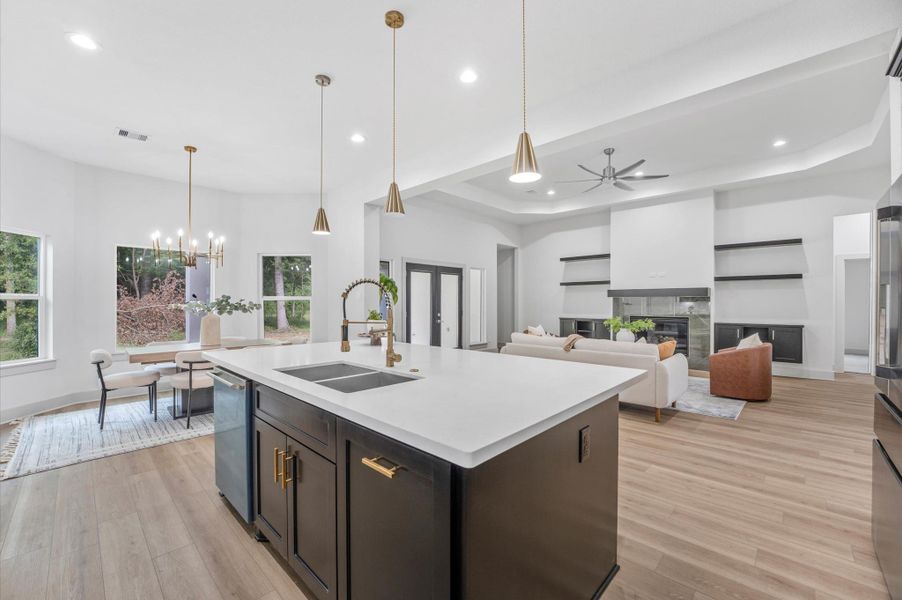 This photo showcases a bright, open-concept living area featuring a modern kitchen with a large island, elegant pendant lighting, and stainless steel appliances. The space flows into a cozy living room with a ceiling fan and a stylish dining area, enhanced by large windows offering natural light and scenic views. This photo showcases a bright, open-concept living area featuring a modern kitchen with a large island, elegant pendant lighting, and stainless steel appliances. The space flows into a cozy living room with a ceiling fan and a stylish dining area, enhanced by large windows offering natural light and scenic views.