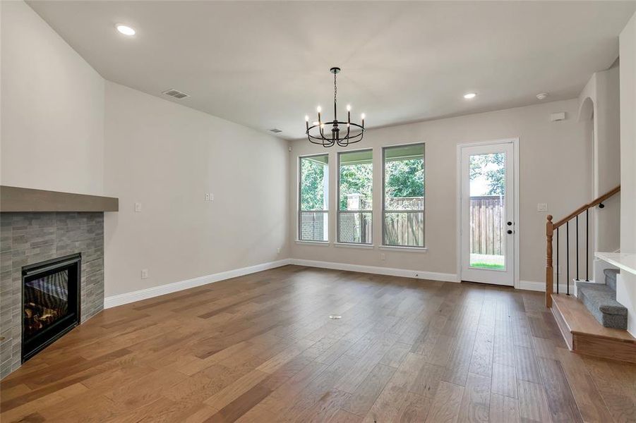 Unfurnished living room with a tiled fireplace, hardwood / wood-style floors, and a chandelier