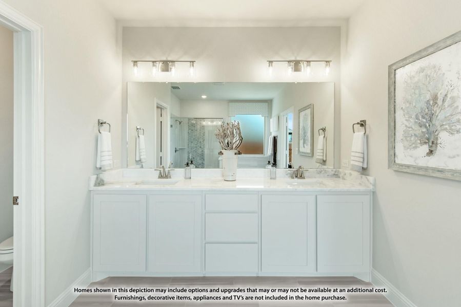 Bathroom with double vanity, white cabinets, marble countertops, large mirror, and walk-in shower visible in background.