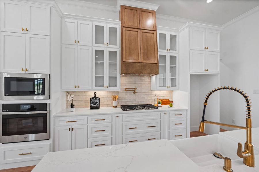 This kitchen boasts elegant cabinetry, a modern gas cooktop, and sleek stainless-steel appliances, complemented by a stylish farmhouse sink and warm wooden accents. Perfect for culinary enthusiasts!