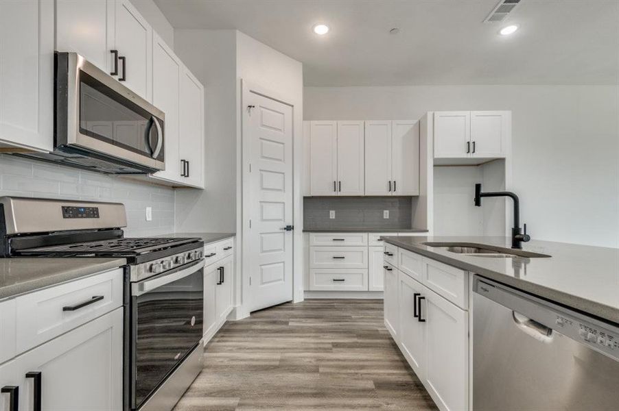 Kitchen featuring backsplash, white cabinets, sink, light hardwood / wood-style floors, and stainless steel appliances