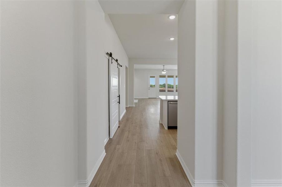 Hallway featuring wood-finish flooring, recessed lighting, and a white barn door with black hardware Hallway featuring wood-finish flooring, recessed lighting, and a white barn door with black hardware