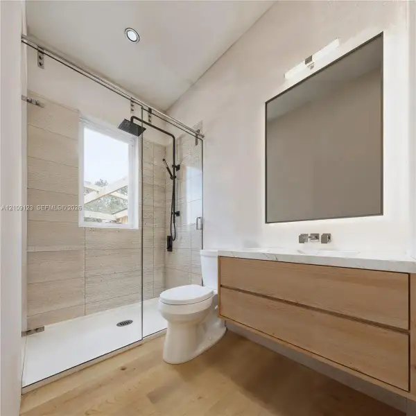 Floating wood-finish vanity with countertop, glass-enclosed shower with matte black fixtures, and recessed lighting Floating wood-finish vanity with countertop, glass-enclosed shower with matte black fixtures, and recessed lighting