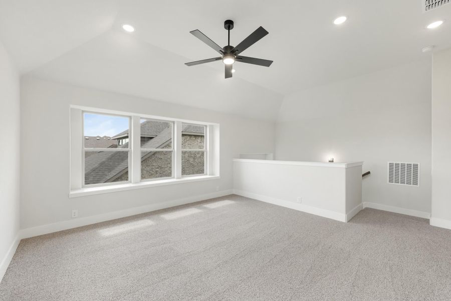 Open upstairs bonus room with vaulted ceiling, ceiling fan, carpet flooring, and staircase railing