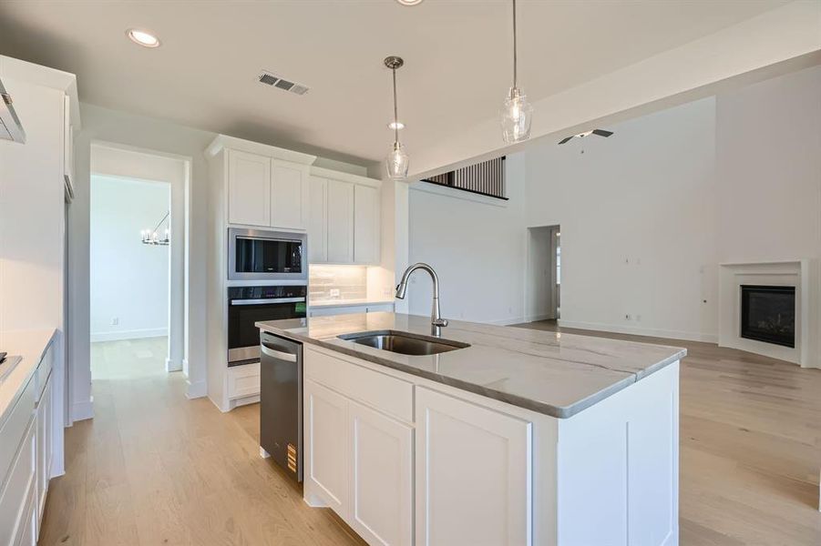 Kitchen with stainless steel appliances, a sink, recessed lighting, light wood finished floors, and light stone countertops
