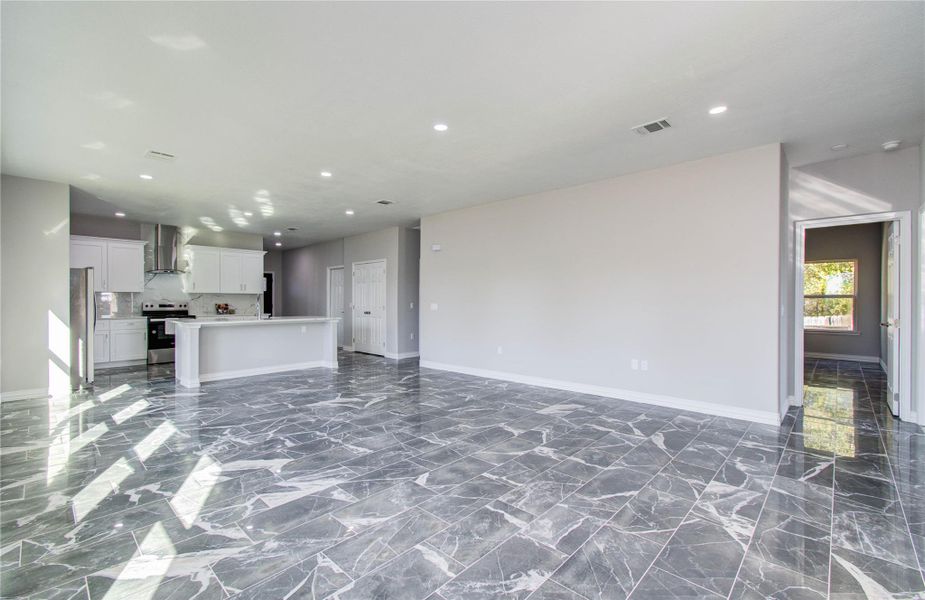 Bright and spacious open-plan living area with modern finishes. Features marble-style flooring and a sleek kitchen with white cabinetry and stainless steel appliances. Ample natural light and neutral walls create a welcoming atmosphere.
