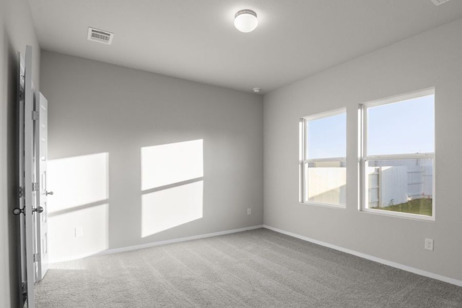 Image of a one story home bedroom with tan carpeting and light grey walls with two windows. Open double doors on left wall