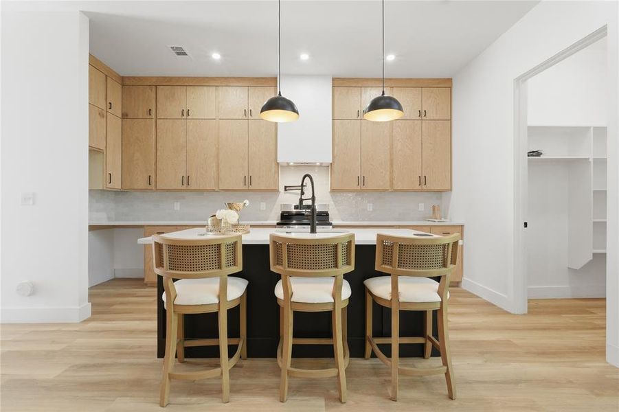 Gourmet kitchen featuring a central island with countertop seating, light wood-finish cabinetry, light-toned countertops, and a full-height tile backsplash