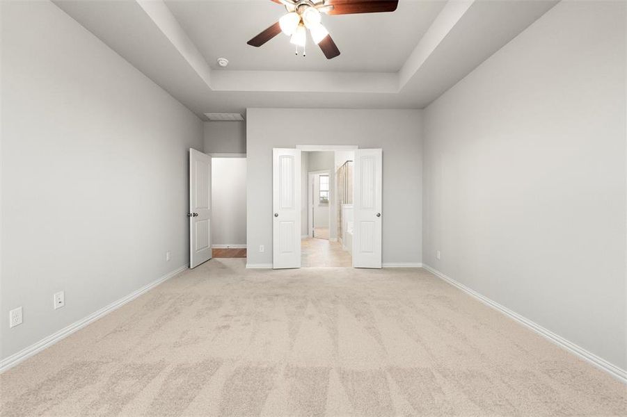 Unfurnished bedroom with a tray ceiling, carpet flooring, and a ceiling fan Unfurnished bedroom with a tray ceiling, carpet flooring, and a ceiling fan