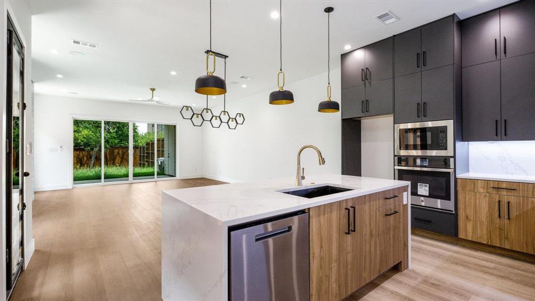 Kitchen with light stone countertops, sink, an island with sink, decorative light fixtures, and appliances with stainless steel finishes