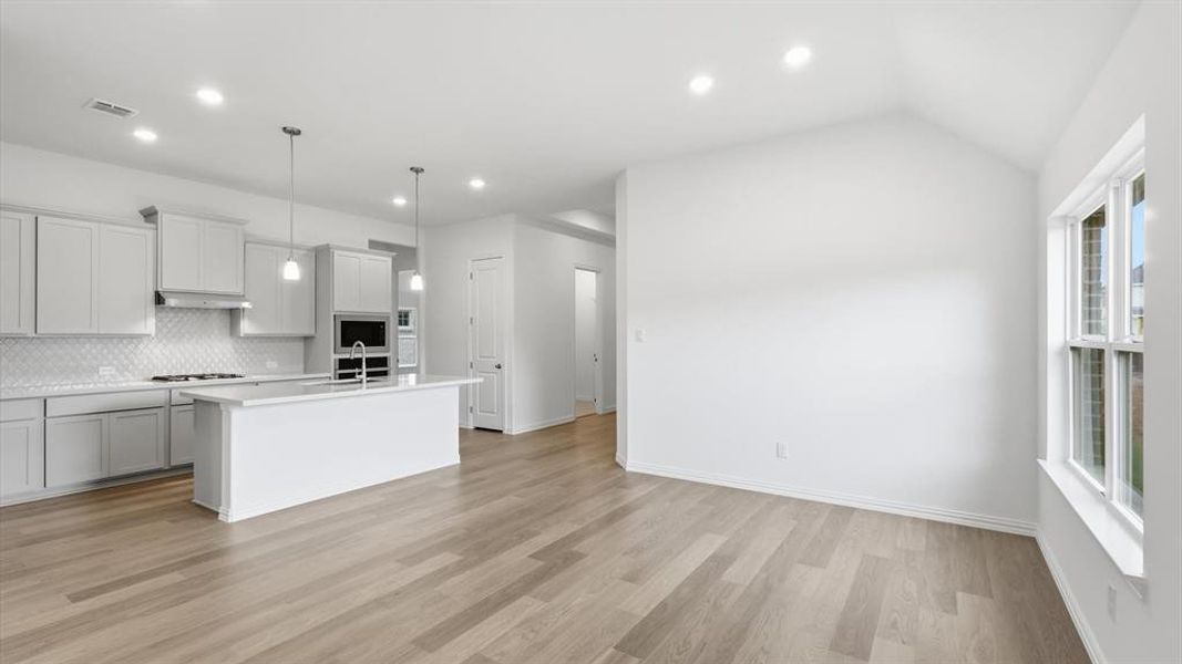 Open-concept living area with light wood-finish flooring, a vaulted ceiling, and recessed lighting Open-concept living area with light wood-finish flooring, a vaulted ceiling, and recessed lighting