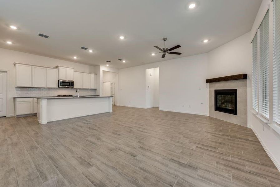 Unfurnished living room featuring a tiled fireplace, ceiling fan, sink, and light hardwood / wood-style floors