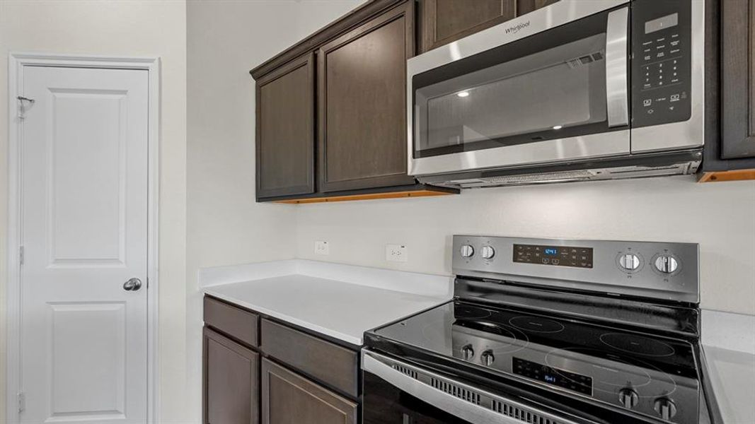Kitchen area with dark wood-finish cabinetry, white countertops, and white walls